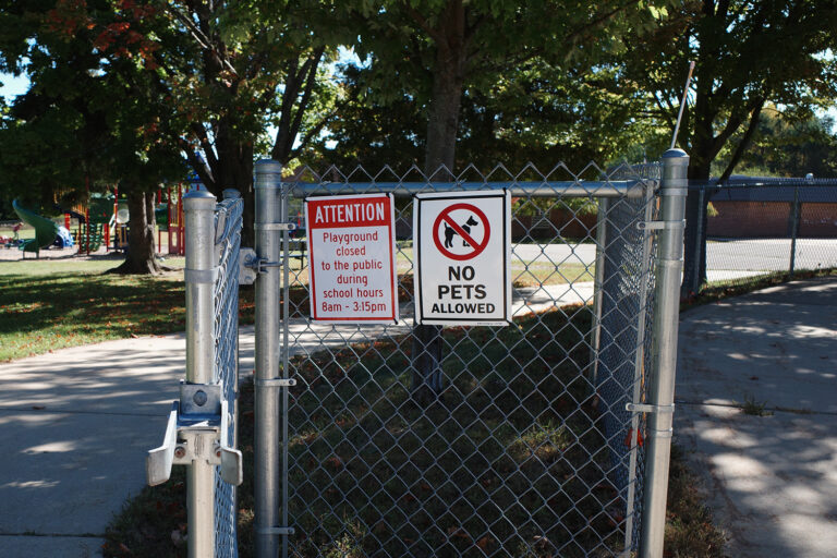 Sign saying "No Pets Allowed" and "Attention playground closed to the public during school hours 8am-3:15pm" outside playground.