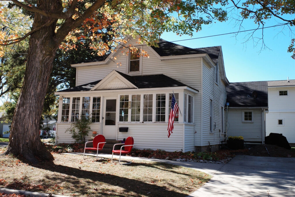 White house with american flag and red chairs in lawn.