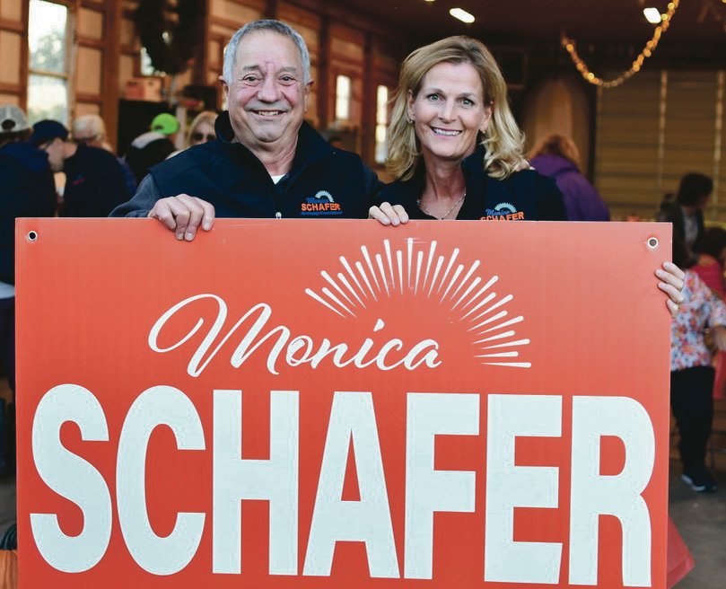 Monica Schafer and supporter pose with "Monica Schafer" sign in red.