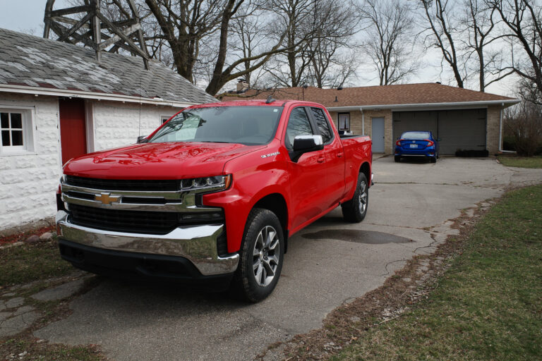 Red truck in driveway with no front blate and blue car in background with back plate