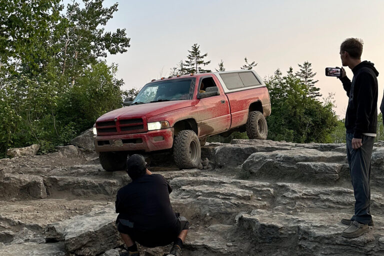 Red SUV traversing off road path as people watch