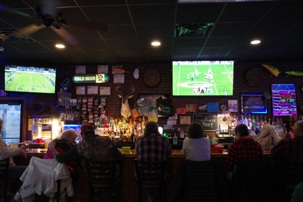 Inside of Chenier's Reef bar with packers game on TVs and people at bar