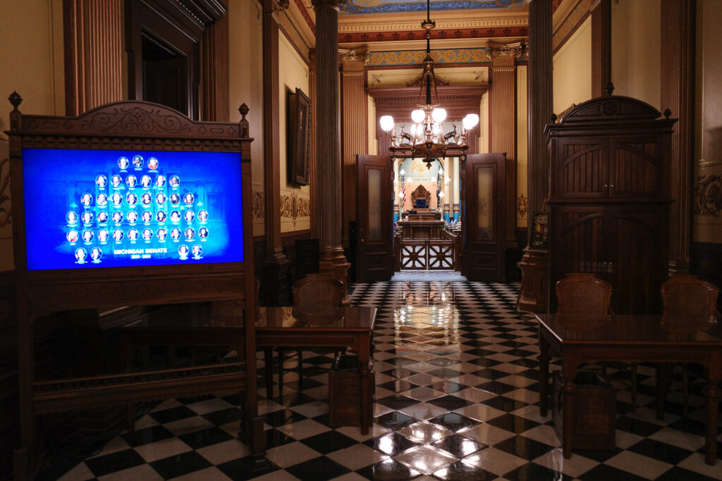 Outside the Michigan Senate chambers with board showing the Senators.