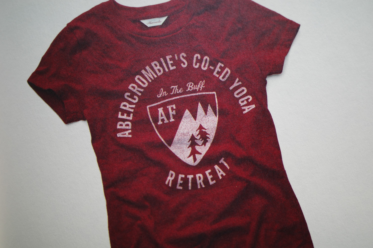 Vintage abercrombie ad with shirt reading "abercrombie's co-ed yoga retreat" and "in the buff"