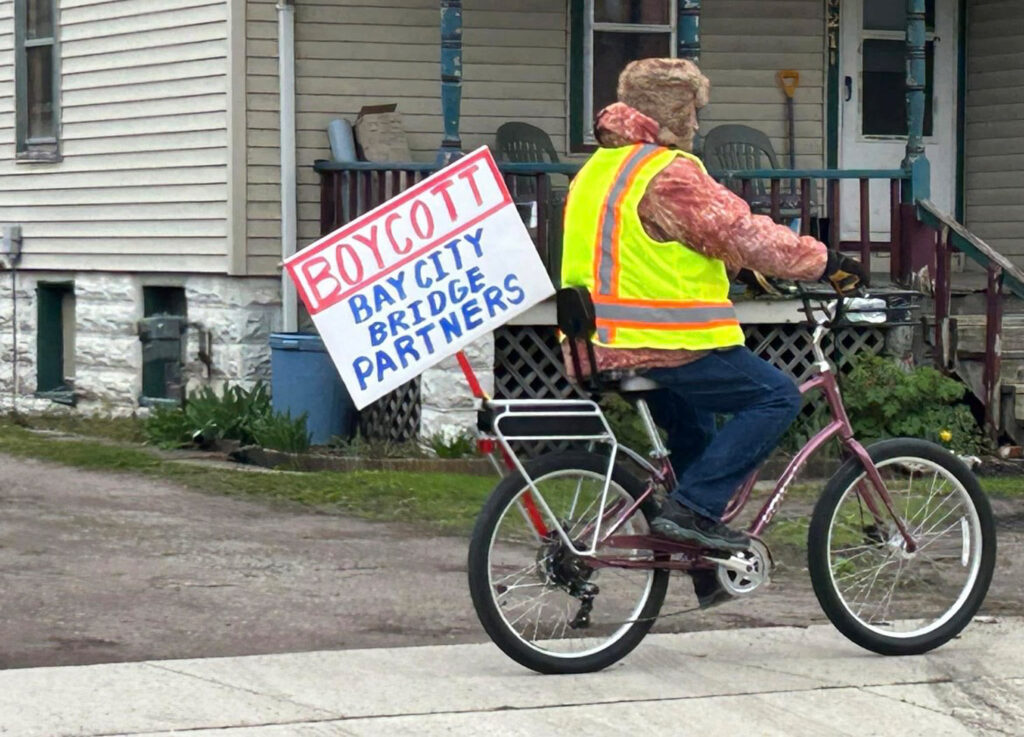 Man on bike with sign reading "Boycott Bay City Bridge Partners"