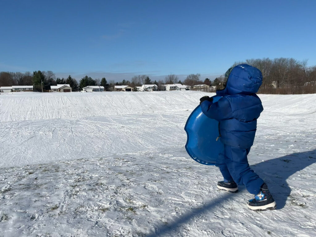 Man approaching snowy hill with sled