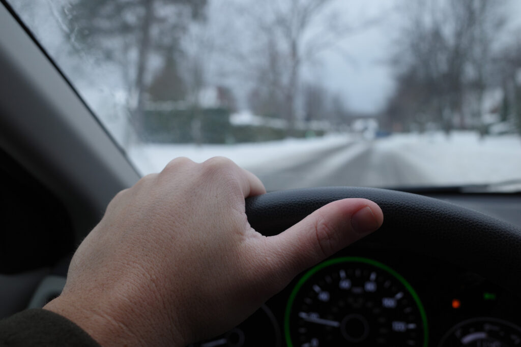 Man's hand on steering wheel overlooking snowy street