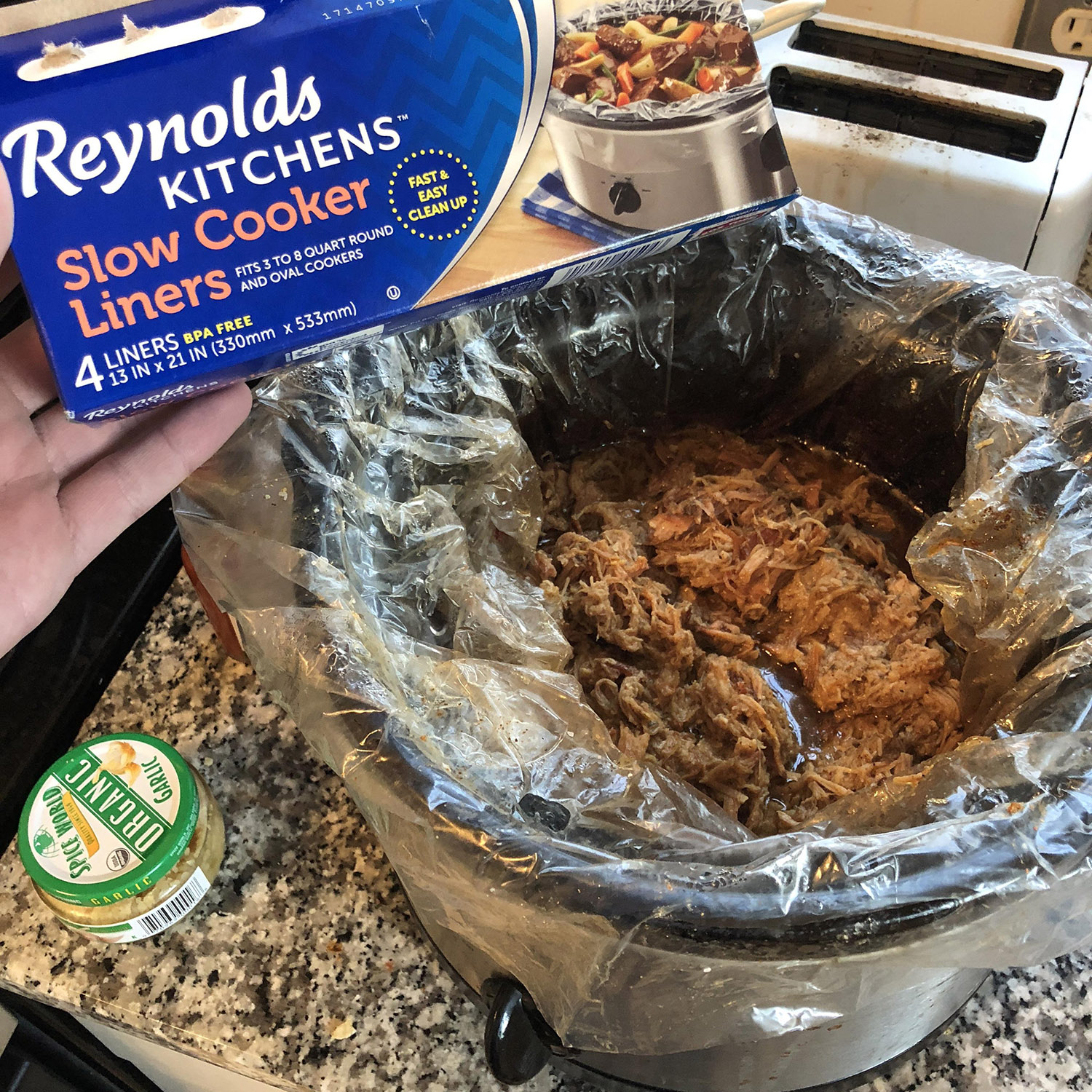 Plastic Reynold's Kitchen crockpot liner with pulled pork next to can of jarlic