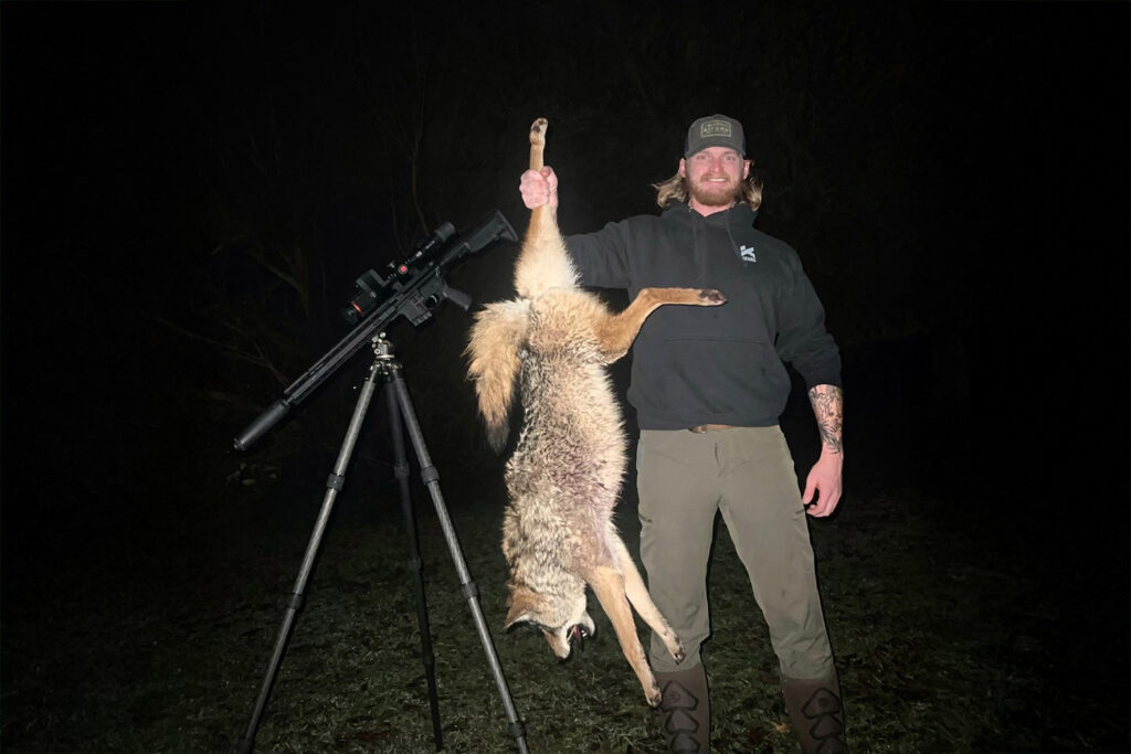 Man posing with rifle and dead coyote