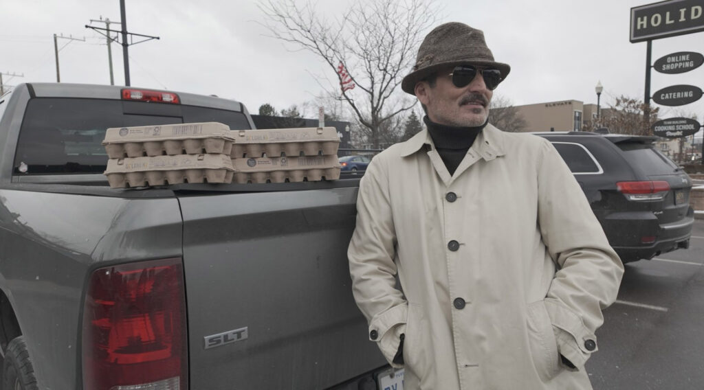 Charlie LeDuff posing in trench coat with egg cartons on truck bed