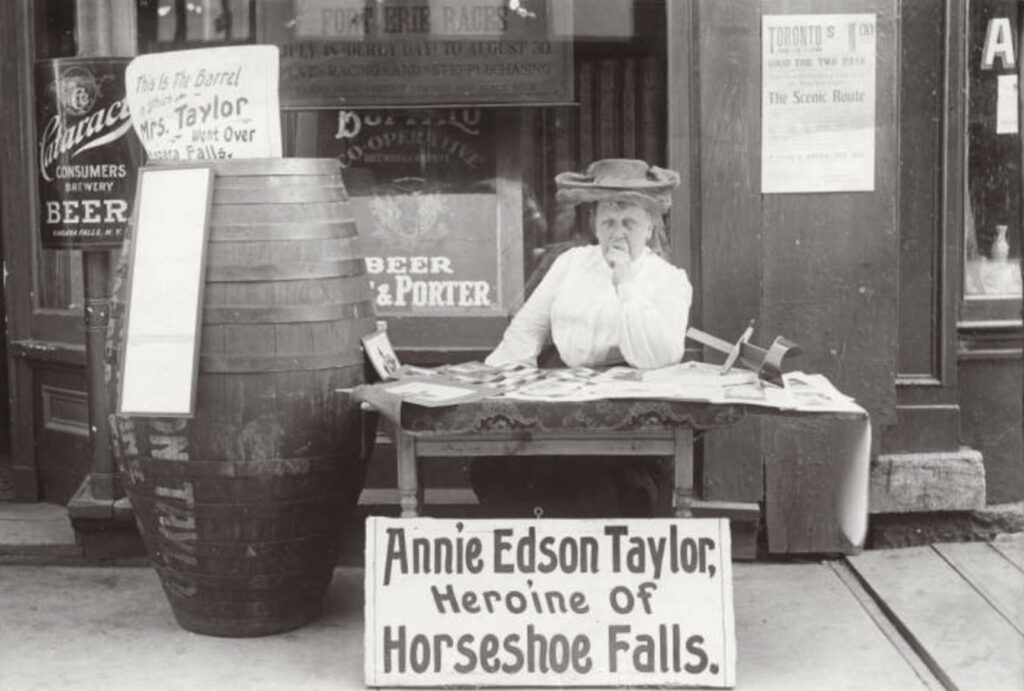 annie taylor with barrel and sign reading "annie edison taylor heroine of horseshoe falls"