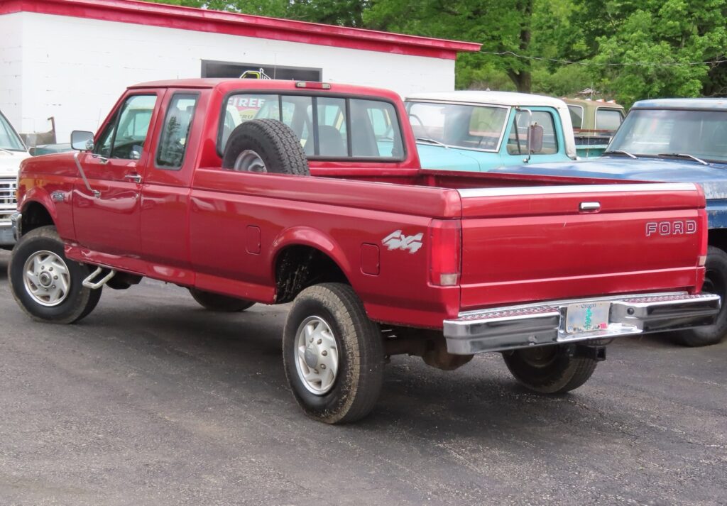 A red 4x4 Ford pickup truck parked in a yard surrounded by other vehicles.