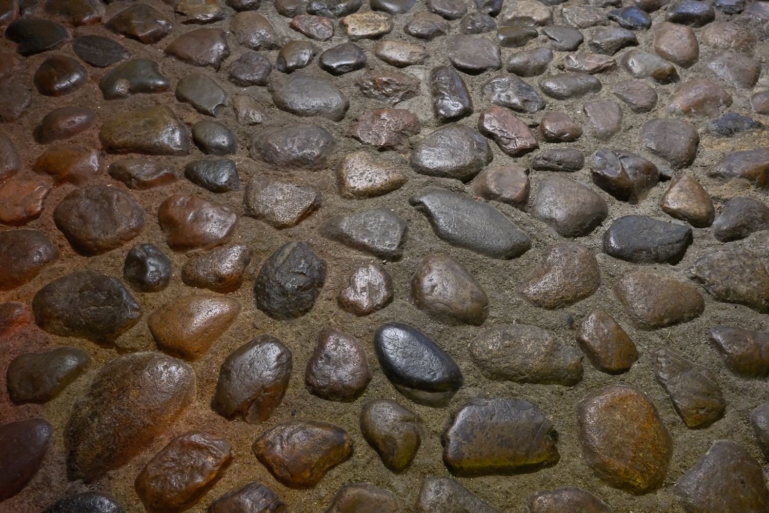 A close-up view of a mosaic made of irregularly shaped river stones or pebbles in shades of brown and gray.