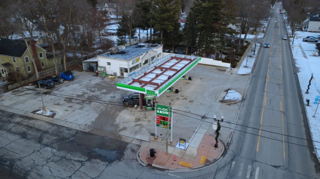 An aerial view of a commercial building with a gas station and several vehicles parked in the lot, surrounded by snowy trees and a road.