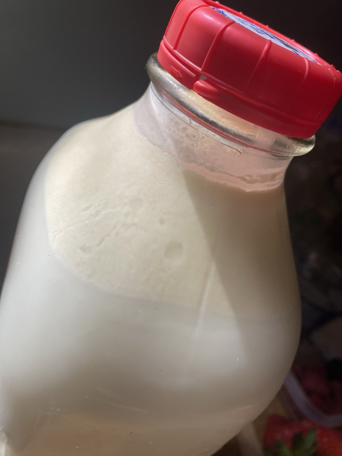 A glass bottle filled with a creamy milk, with a red plastic cap on top.