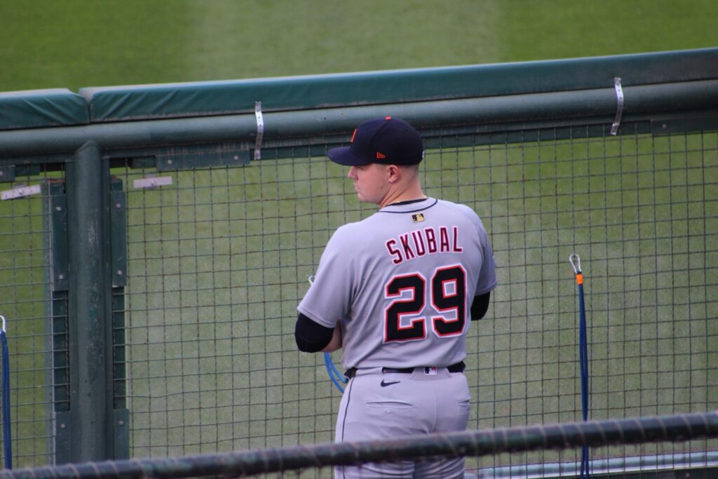 A baseball player in a gray uniform with the name "Skubal 29" on the back standing near a dugout on a baseball field.