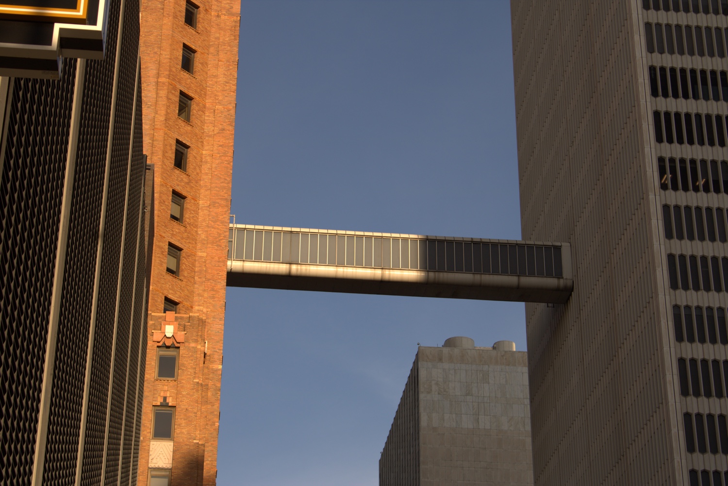 A modern bridge-like structure spans the gap between two tall buildings against a clear blue sky.