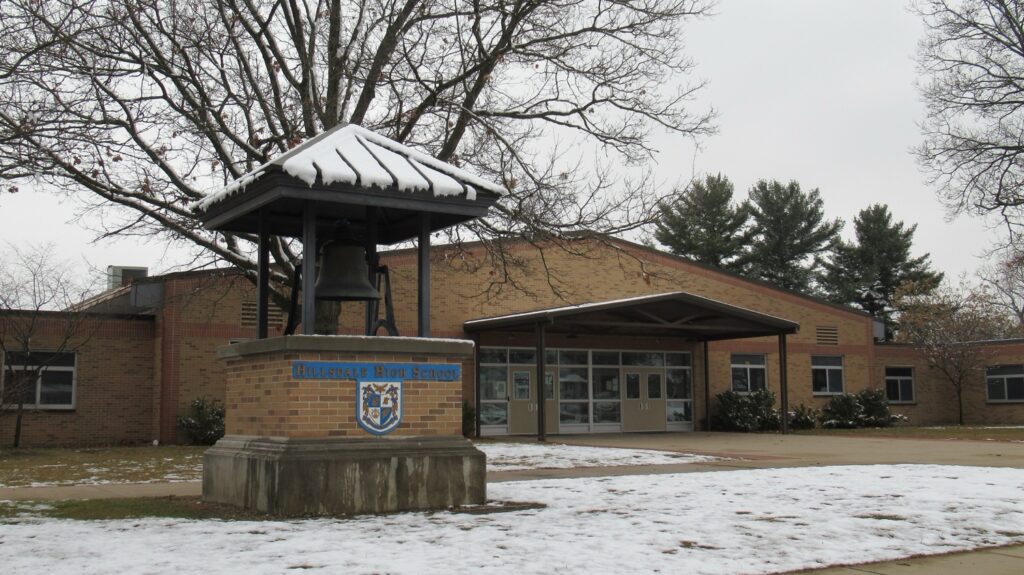 Hillsdale High School, a brick building with a snow-covered roof and grounds, surrounded by snow-covered trees.