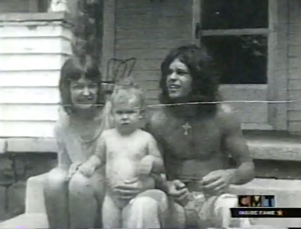 A black and white photograph shows three people, a woman, a man, and a young child, sitting together outdoors.