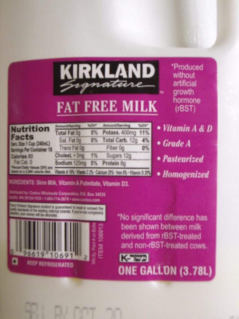 The image shows a one-gallon container of Kirkland Signature fat-free milk, with nutrition facts and product information displayed on the label.