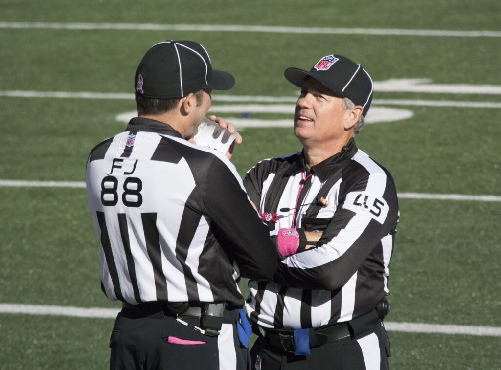 Two referees in black and white striped uniforms standing on a football field, engaged in discussion.