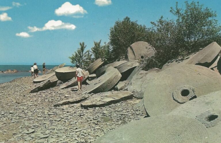A rocky, shoreline landscape with large stone structures along the beach. Several people can be seen walking amongst the rocks.