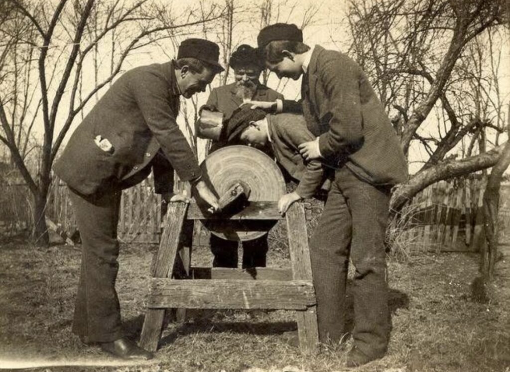 A group of men using a grindstone to sharpen or shape an object in a snowy, forested setting, representative of the town's history as a grindstone production center.