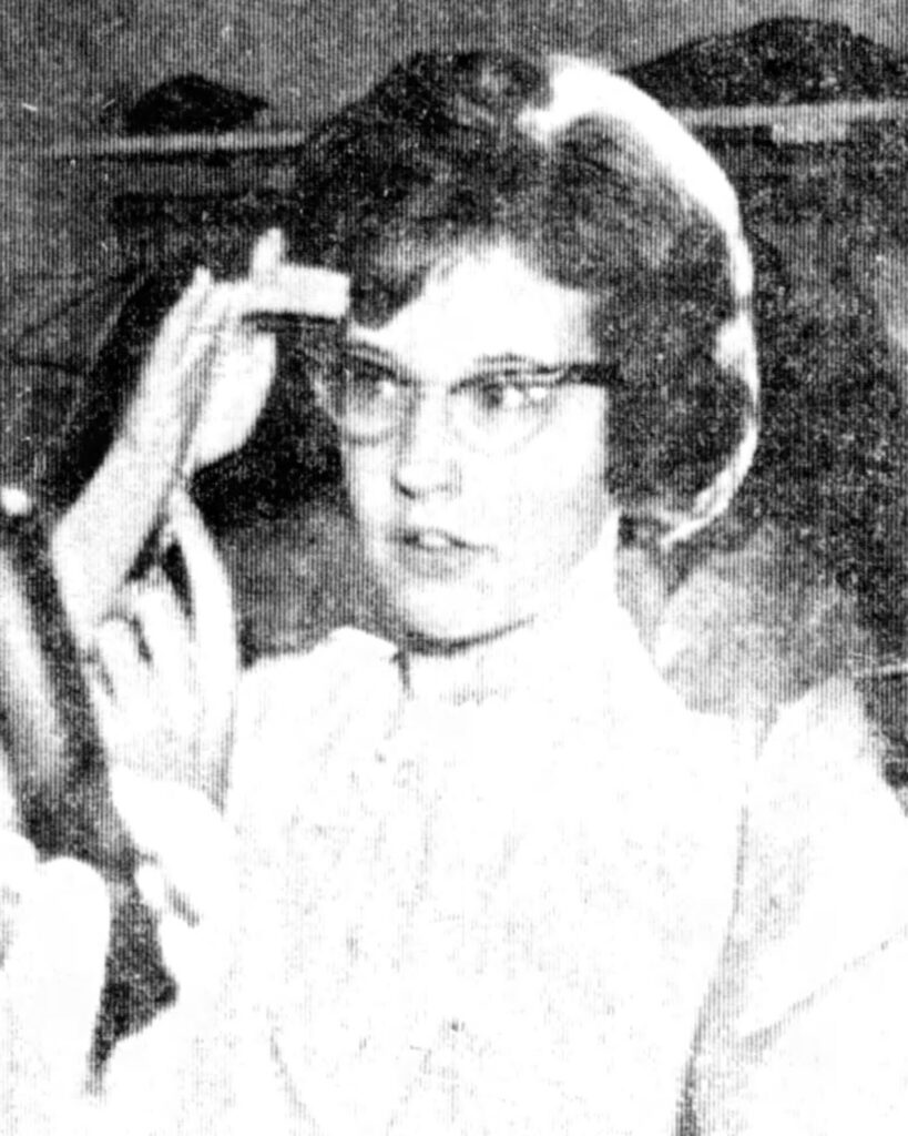 The image appears to depict a portrait of a young individual with short dark hair, wearing a light-colored garment, and set against a blurred background.