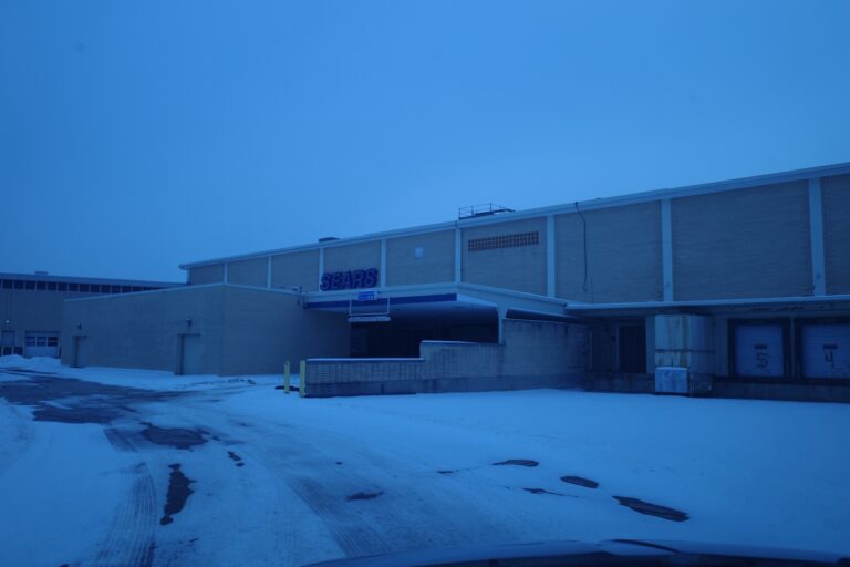 Exterior of a large, abandoned Sears retail store in Livonia, Michigan, with a snowy parking lot in the foreground.