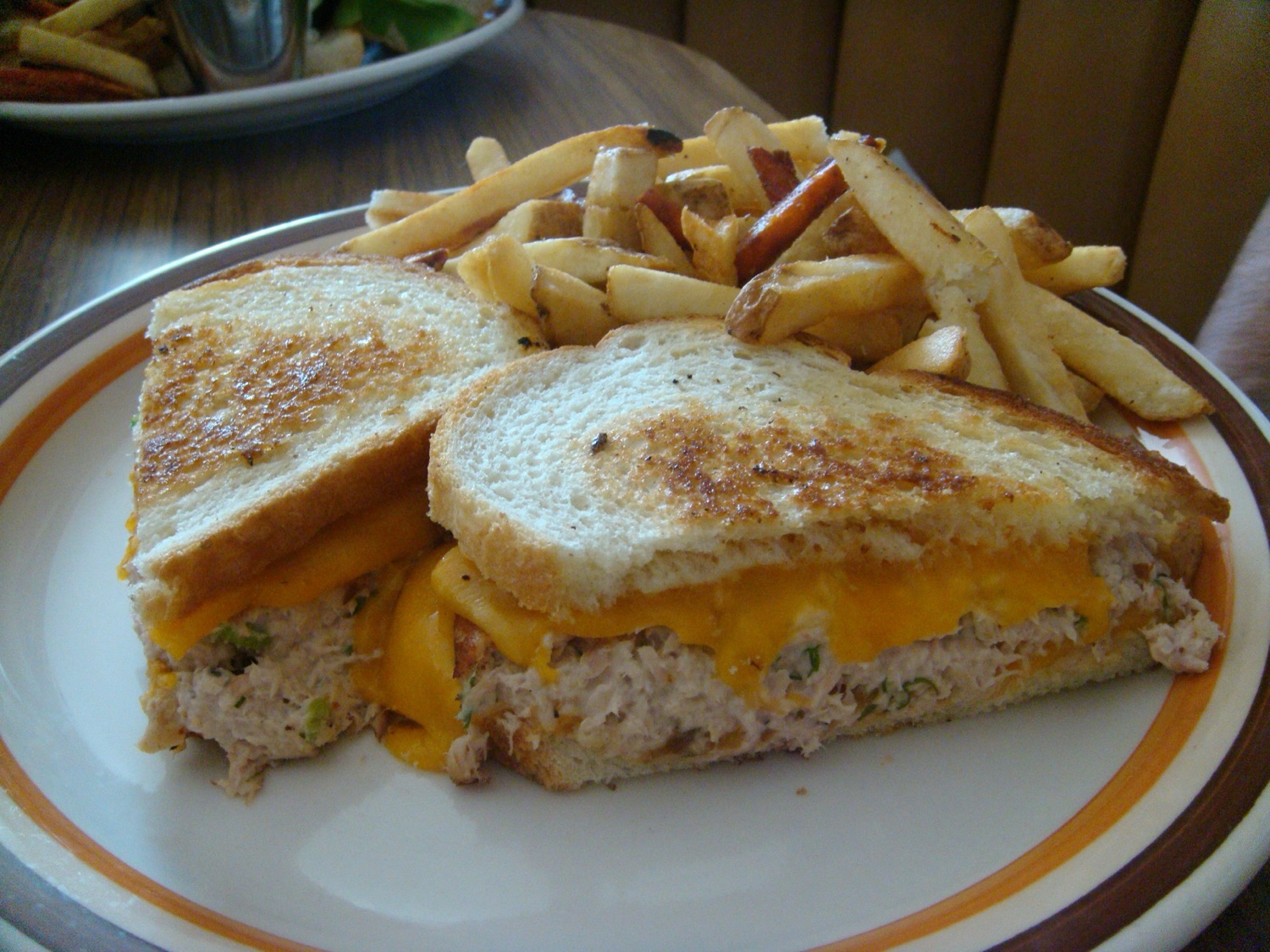 A grilled tuna sandwich with melted cheese, served with a side of french fries on a white plate.