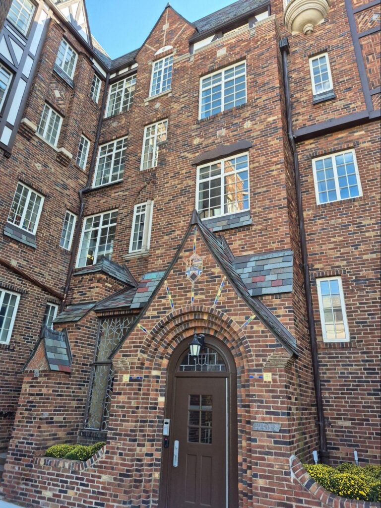The image shows an ornate brick building with a prominent arched entryway, large windows, and decorative architectural elements. 