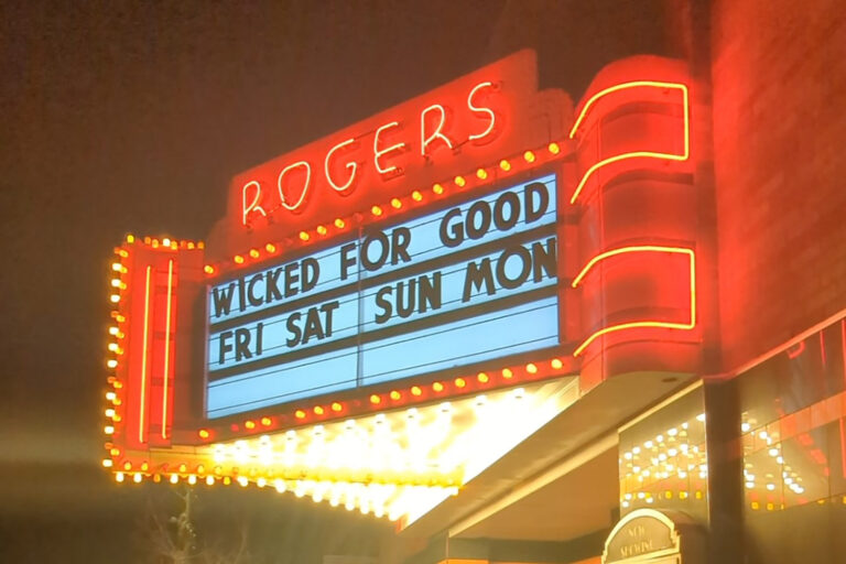 A neon-lit theater marquee displaying the title "Wicked for Good" and showtimes for Friday, Saturday, and Sunday.